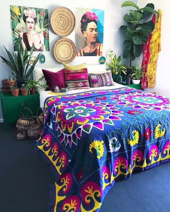 a colorful boho bedroom with a navy carpet on the floor, emerald nightstands, a bold gallery wall, potted plants and bright textiles