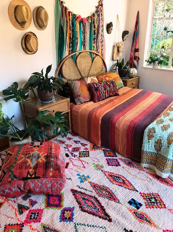 a colorful boho bedroom with bold textiles, pillows, rugs, ottomans and a bunting artwork on the wall is a fun space