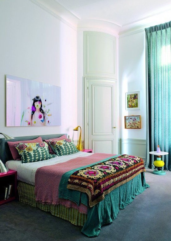 a colorful boho bedroom with bright boho bedding, turquoise curtains, fuchsia nightstands and a green bed plus a bright artwork