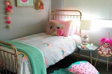 a colorful girl’s room with a metal bed, printed bedding, a bold green rug, fun pillows and cushions, bold art and toys
