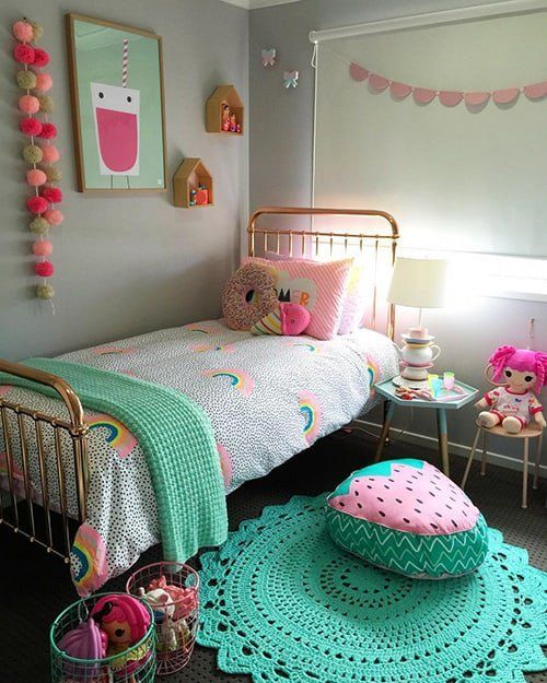 a colorful girl's room with a metal bed, printed bedding, a bold green rug, fun pillows and cushions, bold art and toys