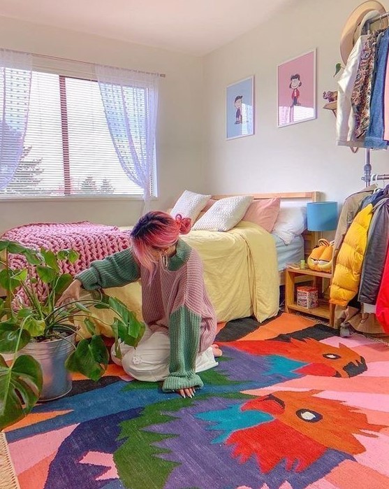 a colorful maximalist bedroom with a bold rug, a bright gallery wall, pastel bedding and colorful curtains plus a potted plant