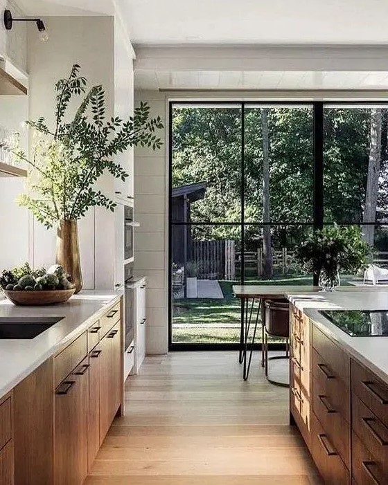 a contemporary kitchen with light-stained cabinets, white stone countertops, a dining space in front of the glazed wall that gives garden views