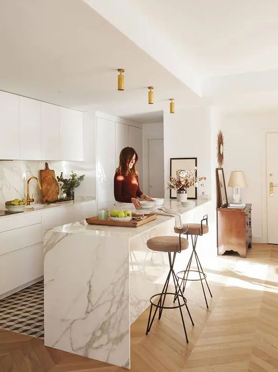 a contemporary white kitchen with sleek cabinets, a white marble kitchen island, matching countertops and a backsplash