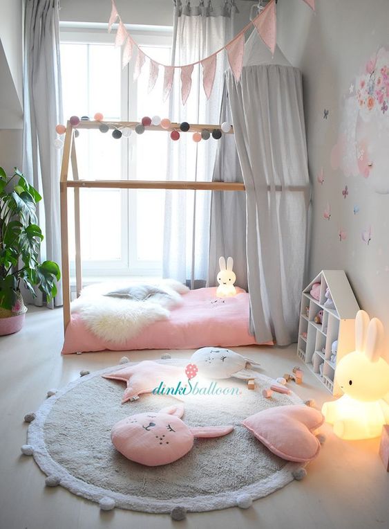 a delicate pastel girl's room with grey walls, a house-shaped bed with pink bedding and a grey canopy, a grey rug and a playhouse
