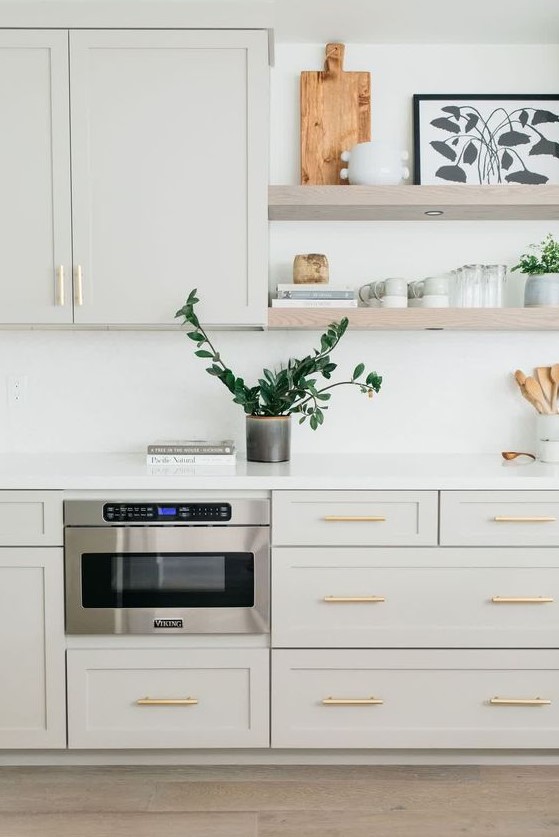 a dove grey kitchen with shaker cabinets, a white backsplash and countertops, floating shelves and gold handles is very elegant