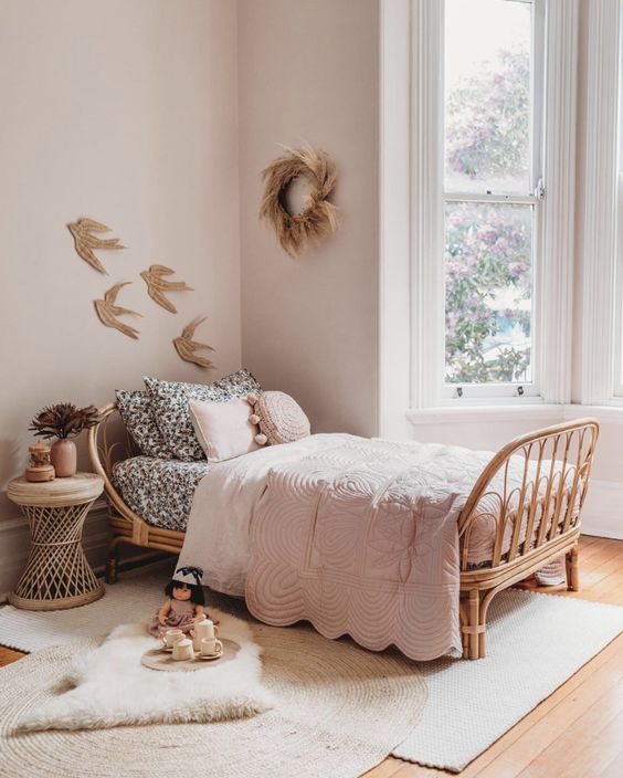 a dreamy boho girl's room with light pink walls, a rattan bed with blush and black and white bedding, layered rugs and a rattan nightstand