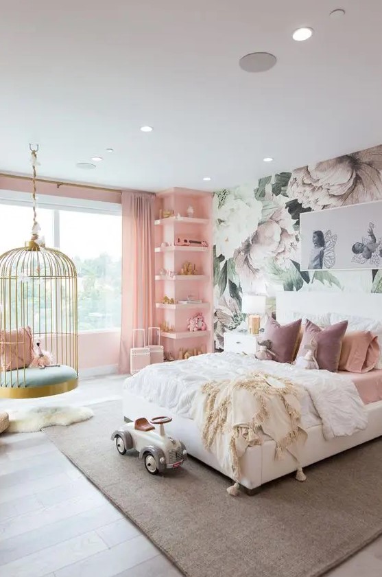 a fantastic girl's bedroom with a floral accent wall, a pink wall with built-in shelves, a white bed with pink bedding, a cage pendant chair