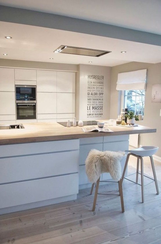 a glam Scandinavian kitchen with sleek cabinets, a storage kitchen island with a wooden countertop, wooden stools and lights