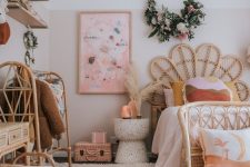 a gorgeous pink boho girl’s room with a light pink clor block, rattan furniture with neutral upholstery, wall-mounted shelves and blooms