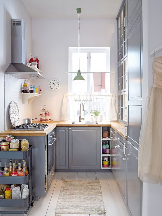 a grey kitchen with butcherblock countertops, a pastel pendant lamp and a grey cart  for additional storage