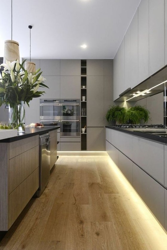 a grey minimalist kitchen with sleke cabinets, black countertops, built-in lights and pendant lamps