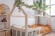 a jungle-themed kid’s room with a house-shaped bed, greenery, a rattan storage unit, some green and mustard bedding