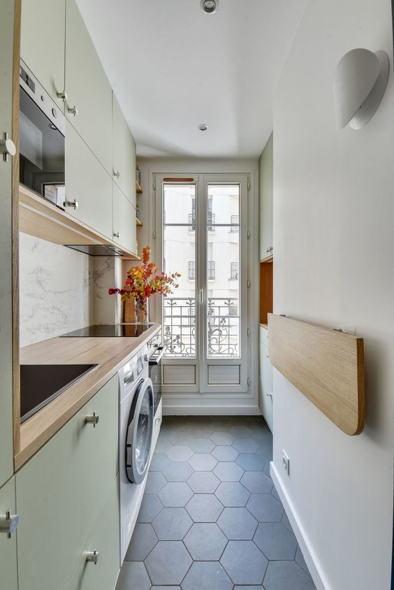 a light green contemporary kitchen wiht butcherblock countertops, a folding mini table and built-in applainces is very chic