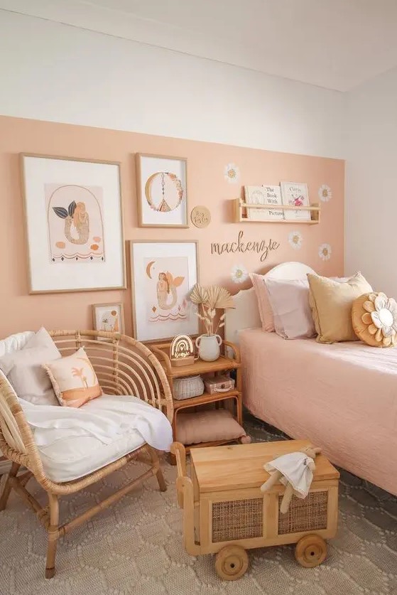 a lovely girl's room with a peachy accent wall and peachy bedding, stained and wicker furniture, a gallery wall and pillows