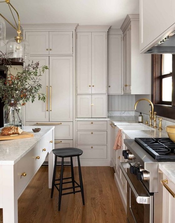 a marvelous creamy kitchen with shaker style cabinets, white quartz countertops and a beadboard backsplash plus gold touches