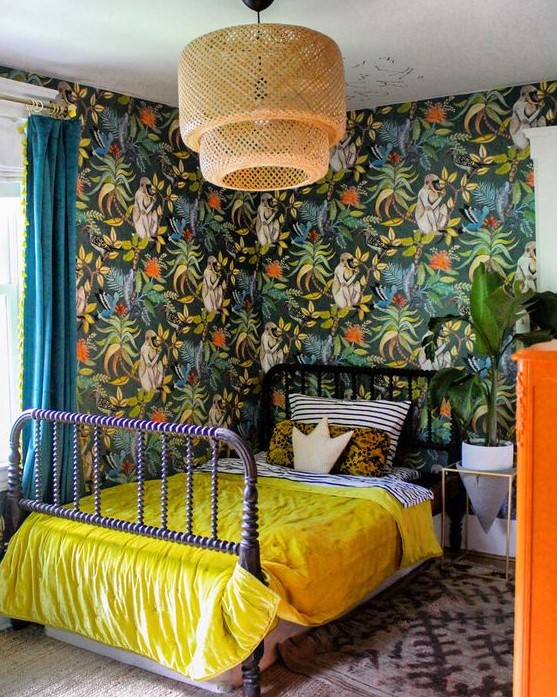 a maximalist space with bold wallpaper walls, a purple bed, a rattan lamp, an orange dresser and bright bedding is chic