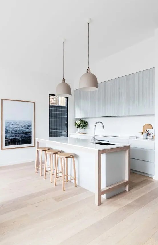 a minimalist beach kitchen with light blue ribbed cabinets and a white kitchen island, wooden stools and pretty pendant lamps