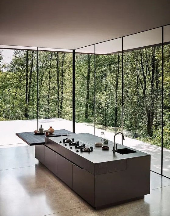 a minimalist grey kitchen with stone coutnertops and an additional built-in mini table plus glazed walls to feel like in the forest