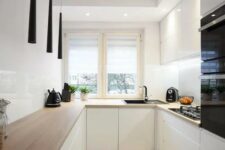 a minimalist white kitchen with butcherblock countertops, a white backsplash and catchy black pendant lamps