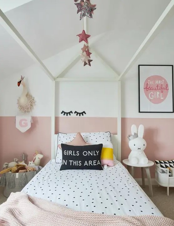 a modern girl's bedroom with color block walls, a white cnaopy bed with polka dot bedding, side tables and a basket with toys