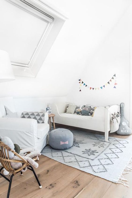 a neutral Nordic bedroom with a neutral bed and grey pillows, a white chair, a printed rug, a grey pouf and pillows