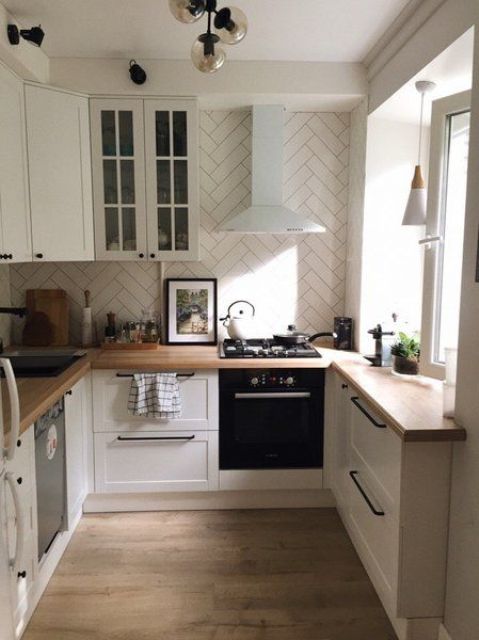 a neutral modern kitchen with a herringbone tiles, butcherblock countertops, black handles and black lamps is cool