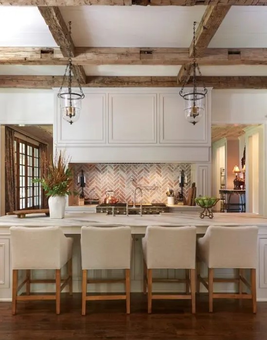a neutral vintage kitchen with chic cabinetry, a large kitchen island, wooden beams and pendant lamps, neutral upholstered stools is very chic and cozy