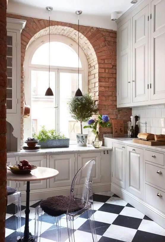 a neutral vintage kitchen with shaker style cabinets, a checked floor, potted greenery, pendant lamps and blooms, clear chairs and a round table