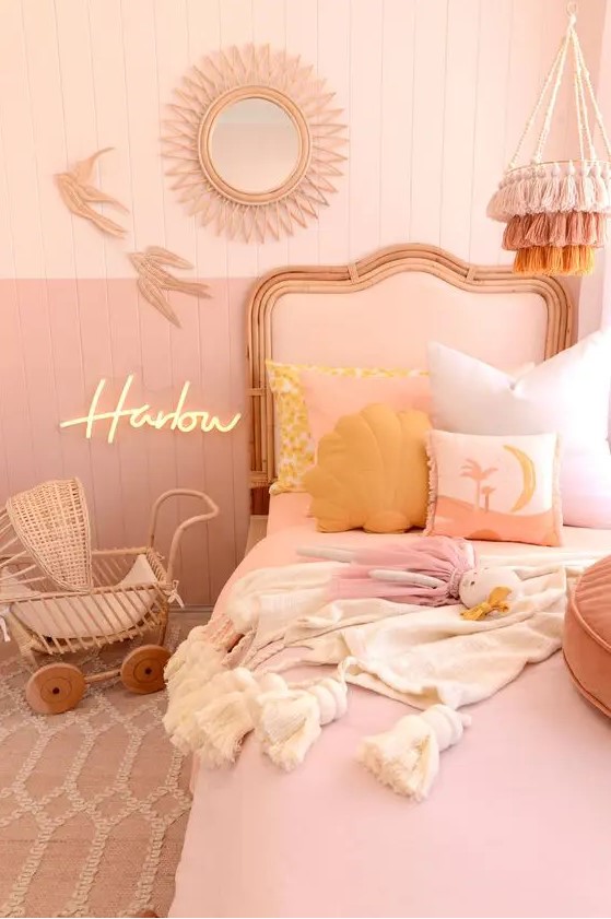 a pink and blush girl's room with color block walls, a blush bed, blush bedding, mellow yellow pillows, a tassel chandelier and a wicker baby carriage