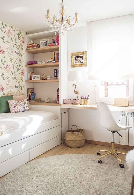 a pretty small girl's room with built-in shelves, a bed with storage, a desk and a white chair, an elegant chandelier