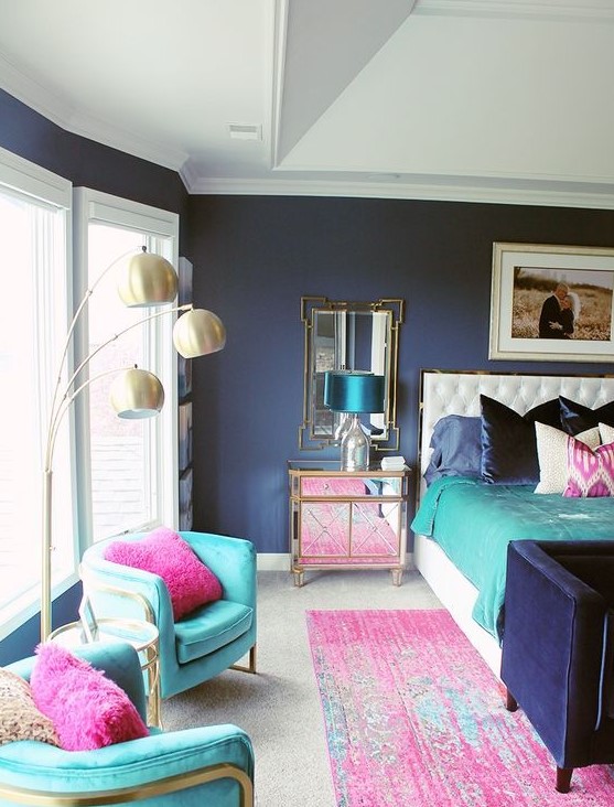 a refined colorful bedroom with navy walls, turquoise chairs, pink pillows and a rug, bold bedding and shiny mirror and metallic touches