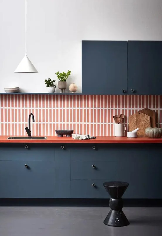 a refined navy one wall kitchen with an orange skinny tile backsplash plus an orange countertop and a white pendant lamp