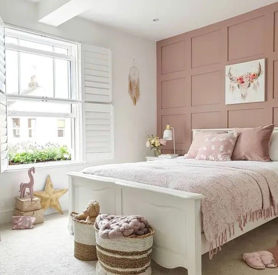 a relaxed and delicate girl's room with a dusty pink wall, a white bed with dusty pink bedding, artwork and pillows is cute