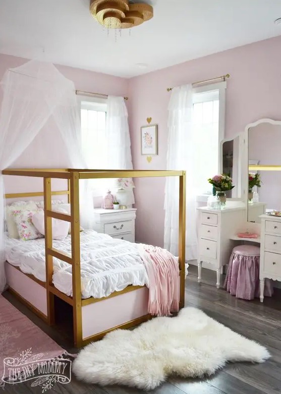 a shabby chic pink girl's bedroom with pink walls, gold canopy beds with pink and white bedding, a vintage vanity and a pink stool