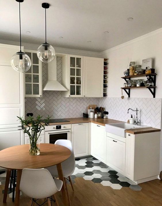 a small and chic neutral kitchen with butcherblock countertops, a white herringbone tile backsplash, pendant lamps and a floor transition