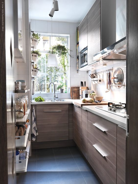 a small brown kitchen with white countertops and a white backsplash, pendant lamps and stainless steel touches