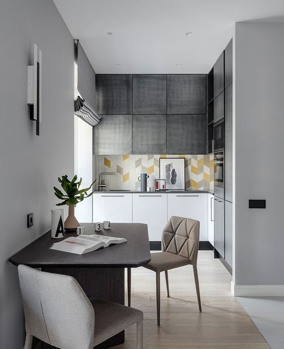 a small contemporary kitchen in grey and white, with a bright tile backsplash, built-in appliances and a dining zone next to it