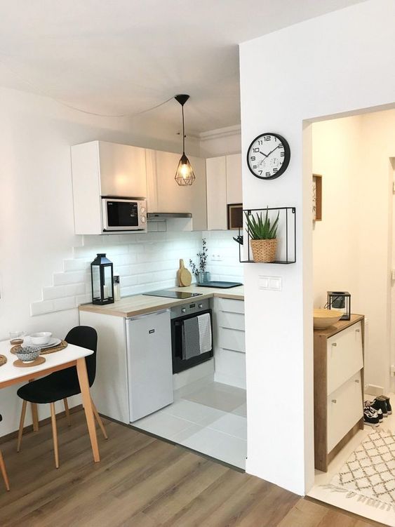 a small minimalist kitchen with white tiles and butcherblock countertops, a table and black chairs plus black pendant lamps