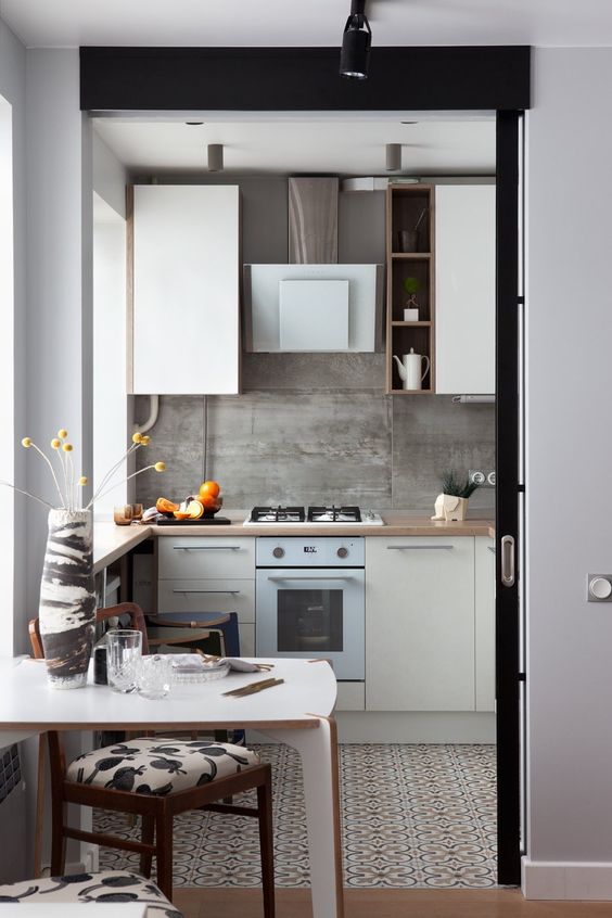 a small modern kitchen with butcherblock countertops, a concrete backsplash and a small table and chairs