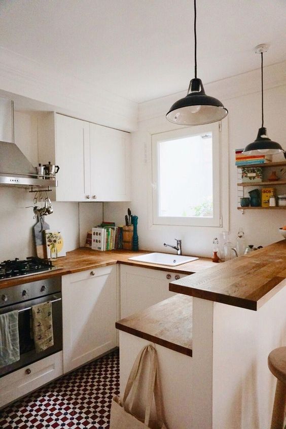 a small modern white kitchen with butcherblock countertops a kitchen island with two tops, retro pendant lamps