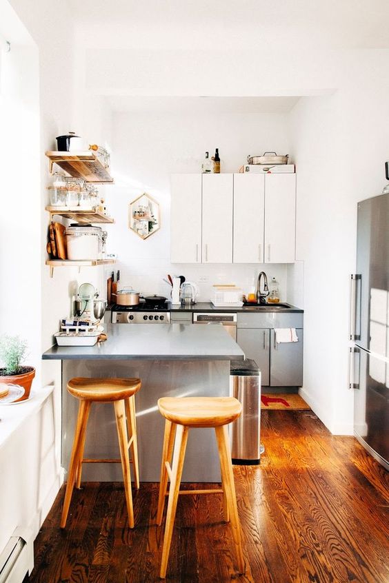 a small two tone kitchen in grey and white, with black countertops, open shelves, tall wooden stools and potted greenery