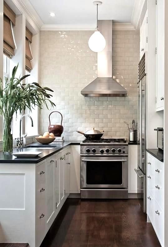 a small white kitchen with black countertops, a white glazed tile backsplash, shades, greenery in a vase and pendant lamps