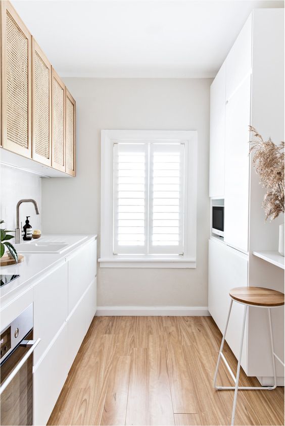 a small white kitchen with sleek cabinets and cane ones, with built-in appliances and a bar counter