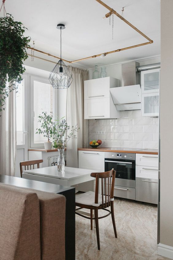 a small white kitchen with stained countertops, a white tile backsplash, a mini folding table and chairs