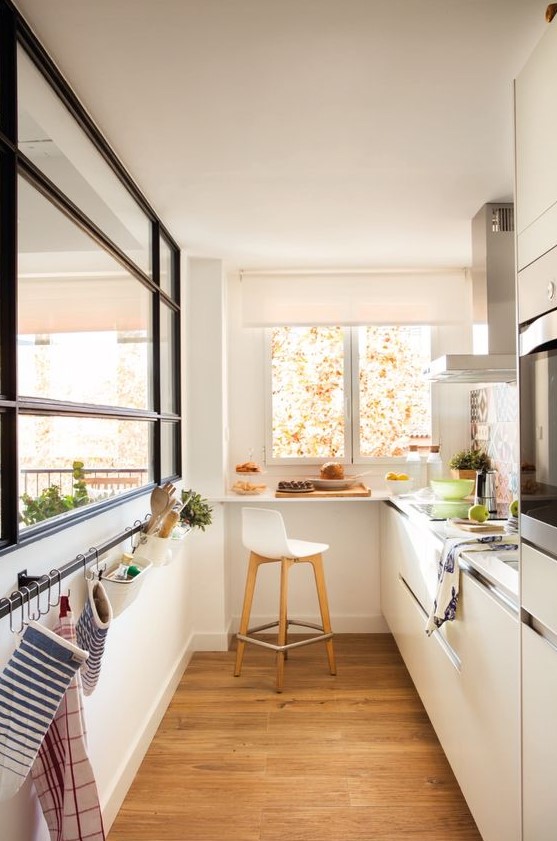 a small yet welcoming white minimalist kitchen with neutral countertops, a large window, a holder for towels and a windowsill bar