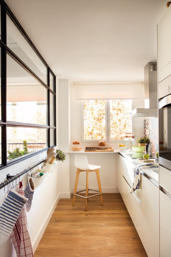 a small yet welcoming white minimalist kitchen with neutral countertops, a large window, a holder for towels and a windowsill bar