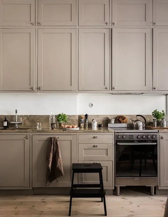 a stylish and moody taupe kitchen with shaker style cabinets, elegant appliances and a grey stone backsplash and countertops is very elegant