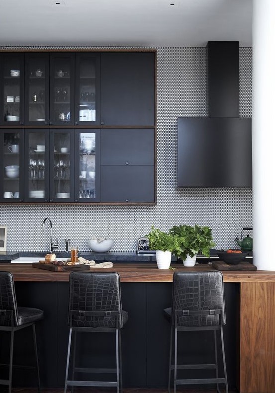 a stylish kitchen with graphite grey cabinets, a wooden kitchen island, black leather stools and a black hood
