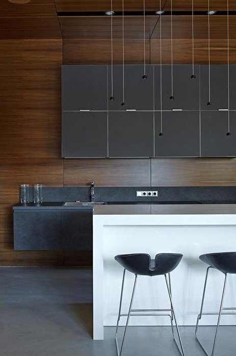 a super stylish minimalist kitchen with matte grey cabinets, stone countertops, a white kitchen island plus black stools